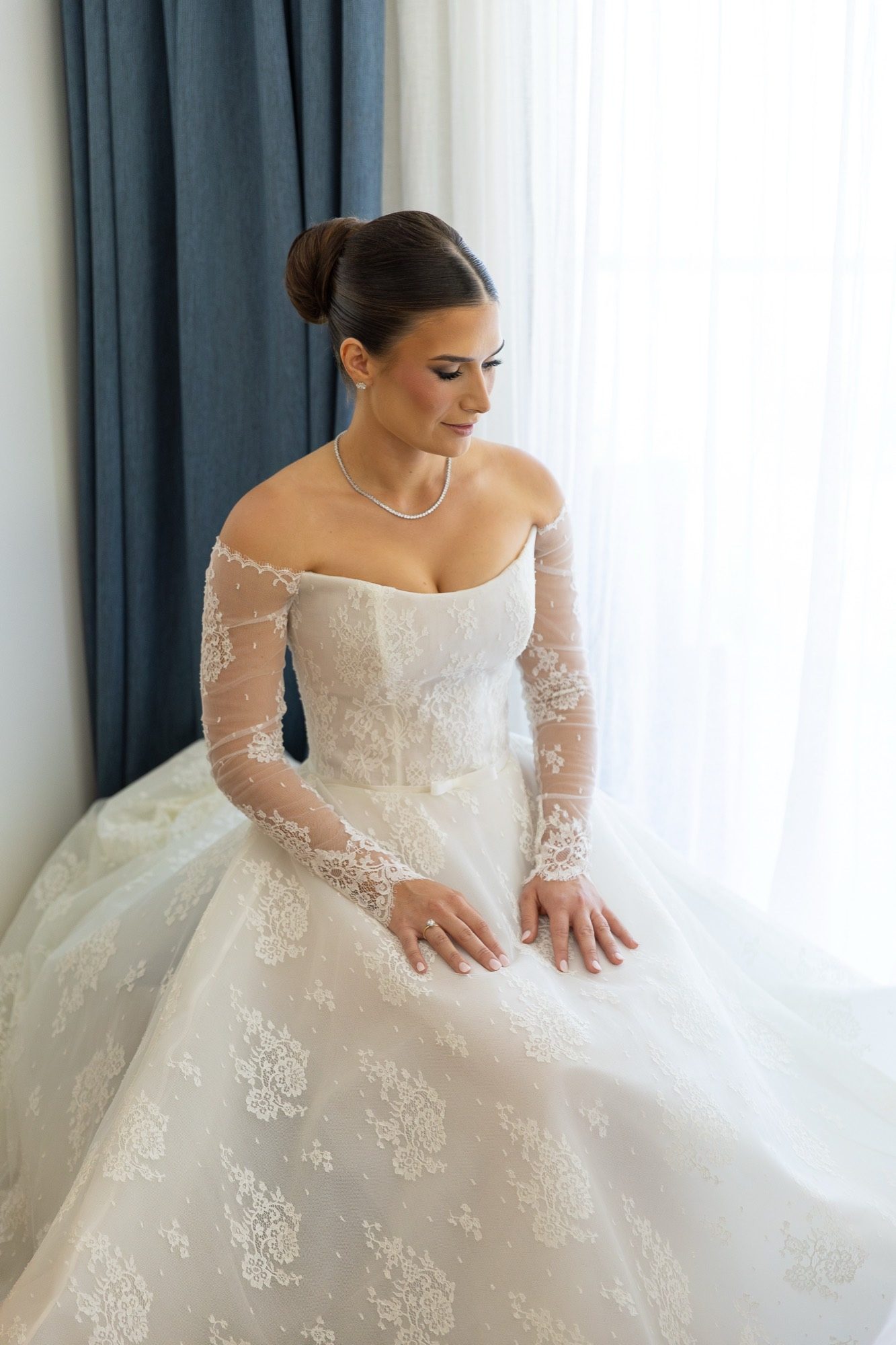 The bride seated by the window in an off-shoulder Chantilly lace gown before the ceremony, Freedom Shores, Airlie Beach