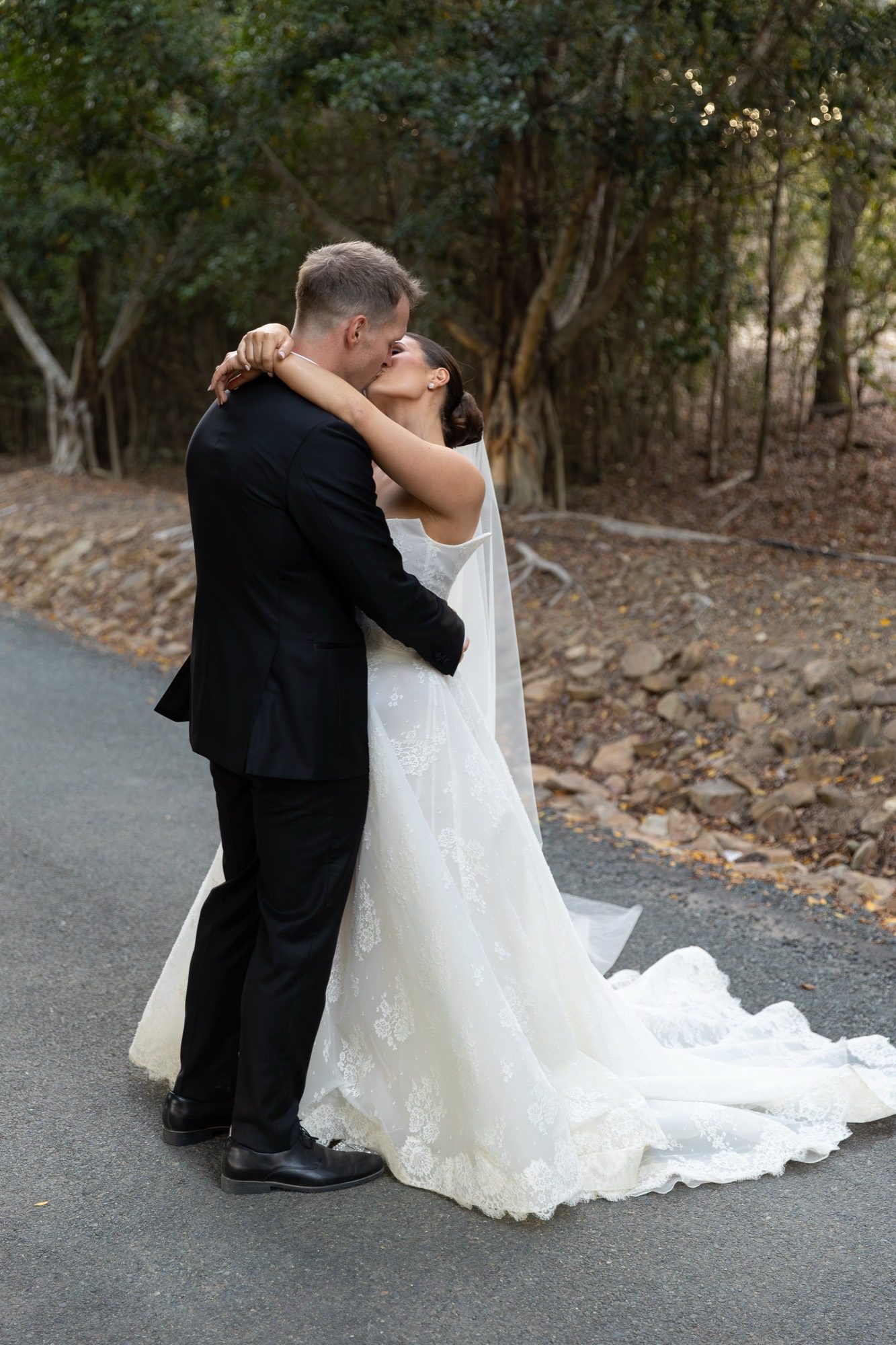 The couple kissing on a quiet bush road, veil trailing, Airlie Beach